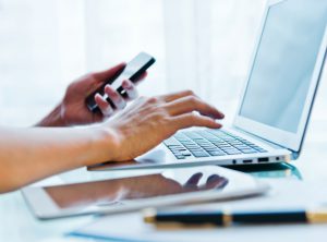 Man inputing data on laptop and holding mobile phone in another hand.