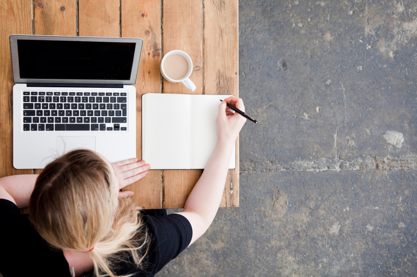 Top view of woman taking notes and studying from laptop