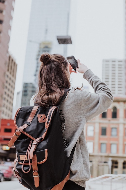 Woman with backpack looking up and taking photos of buildings